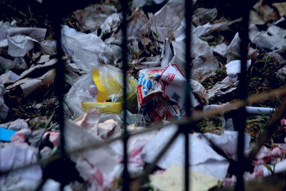 A collection of multiple plastic rubbish bags filled with waste, stacked against a white exterior wall on a cobblestone pavement. The bags are in various colors, including yellow, white, and transpare